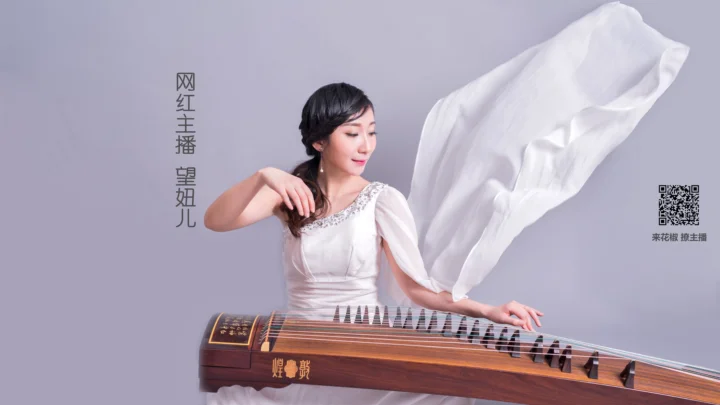 一位身穿白色服装的成年女性坐在古筝旁，身后白色布料飘动，背景为浅灰色。