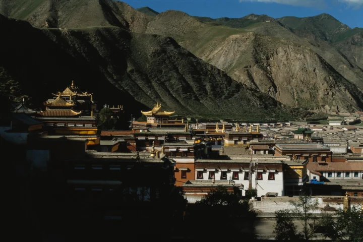 山谷中的藏式寺院建筑群依山而建，背后是陡峭的褐色山脉。