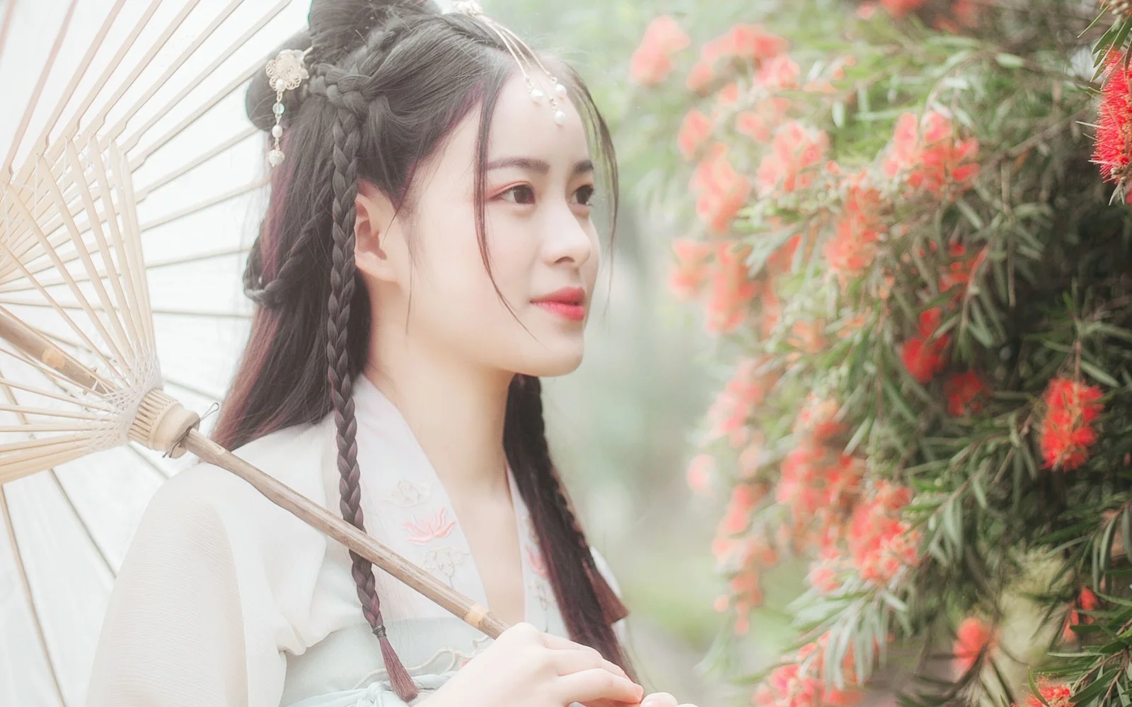 연한 전통 의상을 입은 여성이 종이 우산을 들고 꽃 옆에 서 있다.