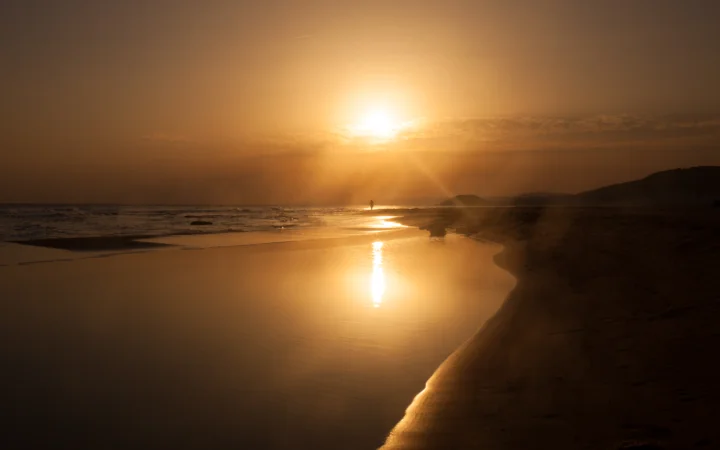 金色夕阳照耀着海滩与海面，水中的光影倒映出温暖宁静的景色。