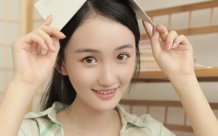 一位年轻女性在室内手持书本微笑面对镜头。