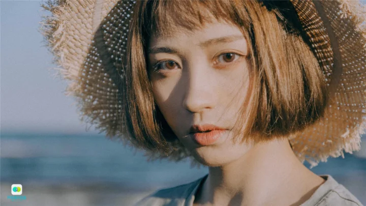 一名戴草帽的女性在海边的柔和光线下看向镜头。