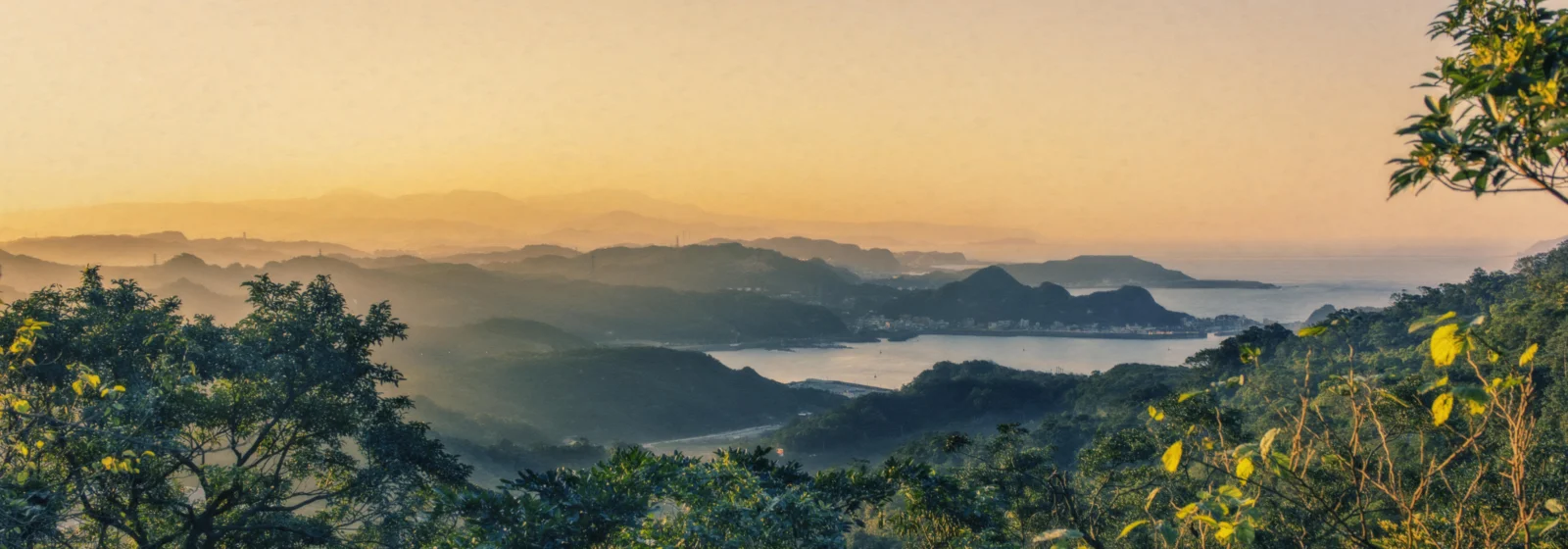 노을빛에 물든 겹겹의 산과 호수, 숲이 펼쳐진 고요한 와이드 풍경입니다.