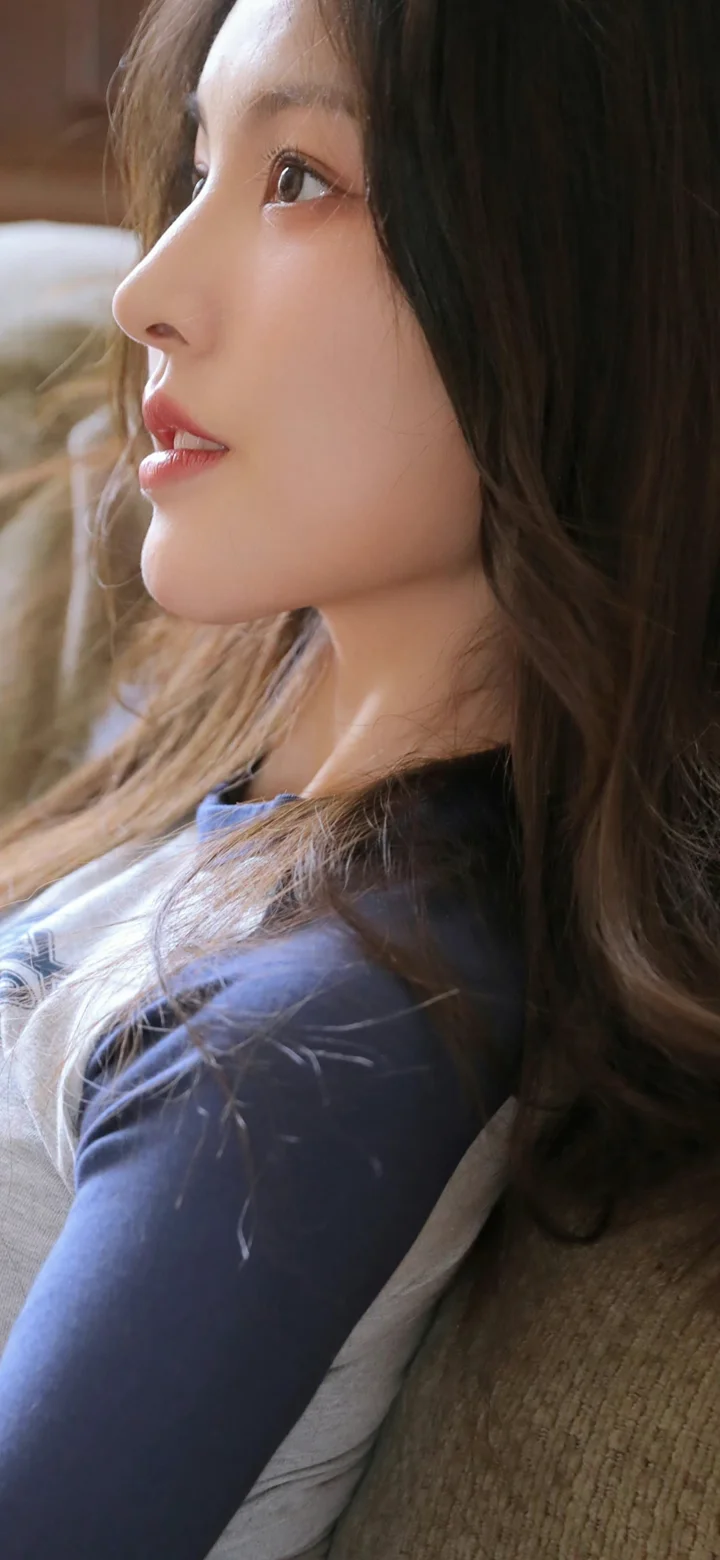 一位长发女性身穿深色上衣，呈侧脸近景。
