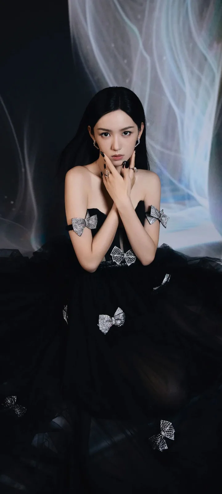 一名成年女性身穿黑色礼服，在深色背景前交叉双手摆出肖像姿势。