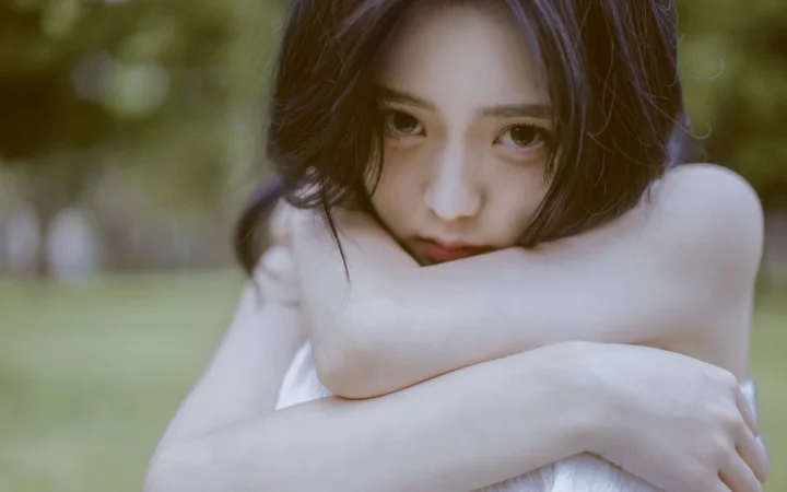一名女性在户外绿意背景前抱臂凝视镜头。