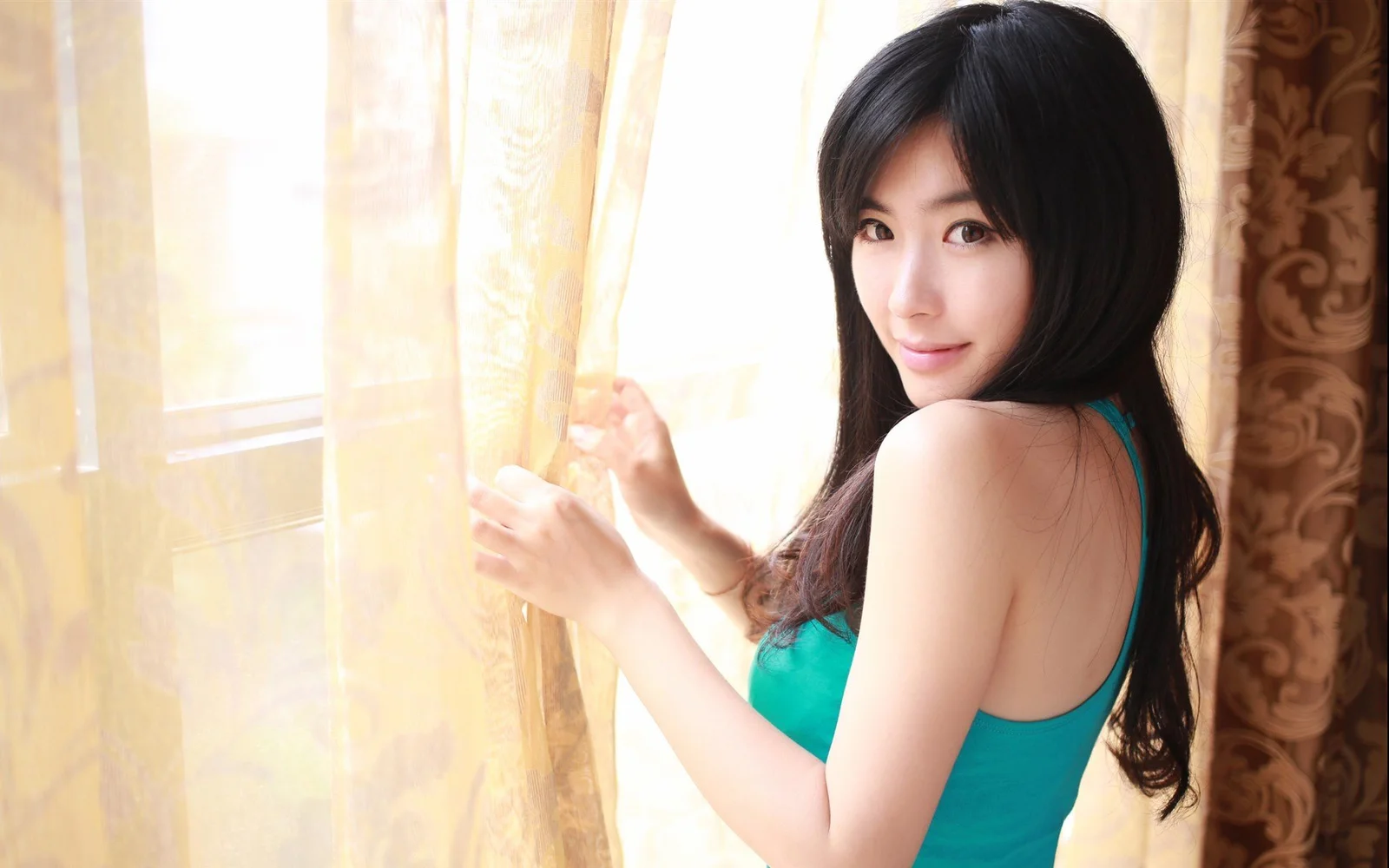 一名女子站在窗边，手扶着浅色窗帘并回头看向镜头。