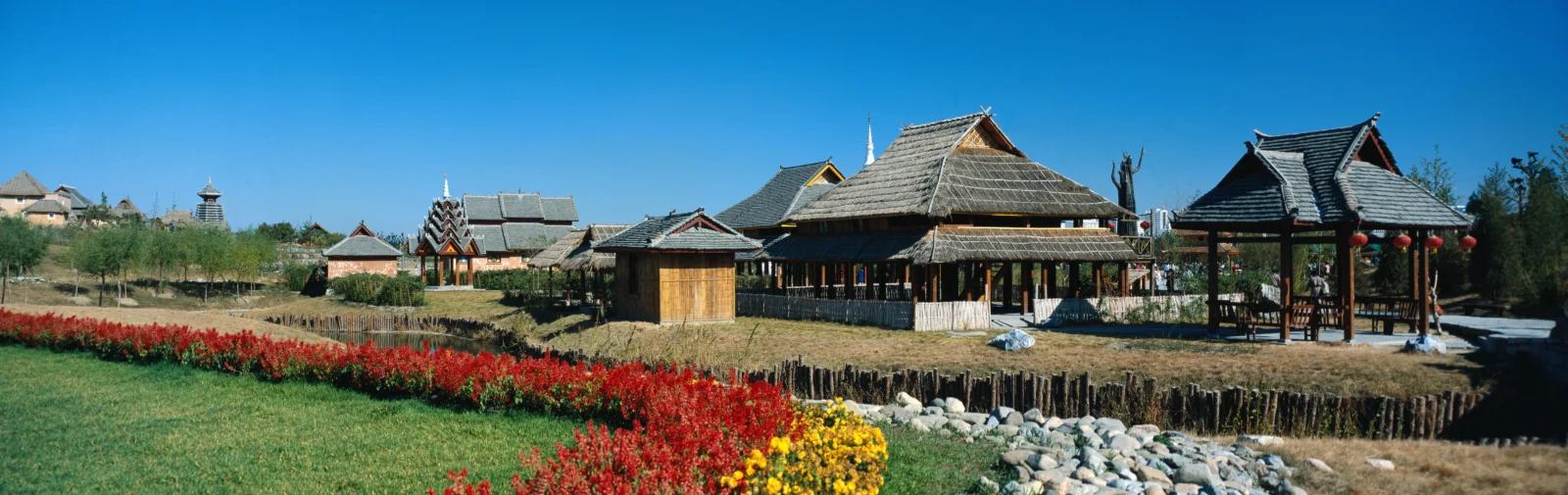 藍天下的傳統木結構建築群前是整齊的紅色花卉、草地和石景。