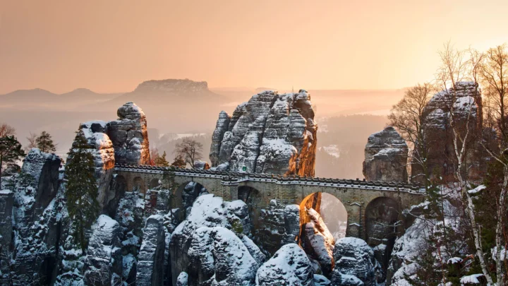 夕阳映照下，积雪覆盖的岩石峰林与石拱桥构成冬日风景。