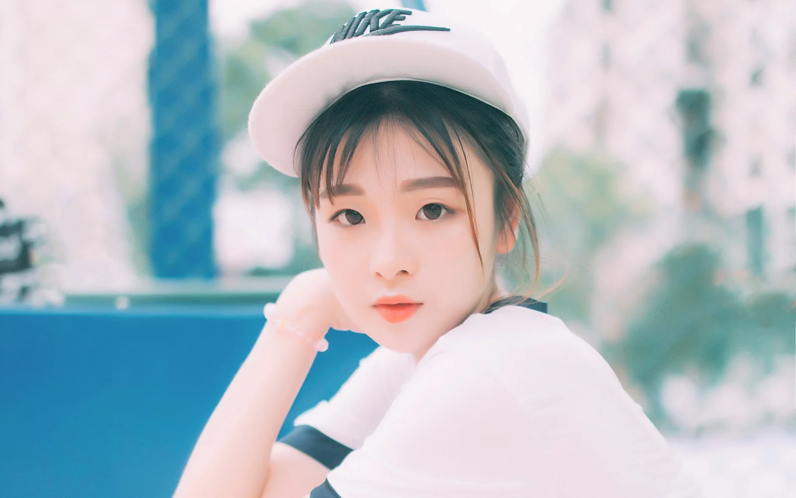 흰 모자와 흰색 상의를 입은 여성이 부드럽게 흐려진 배경 앞에서 카메라를 바라보고 있습니다.