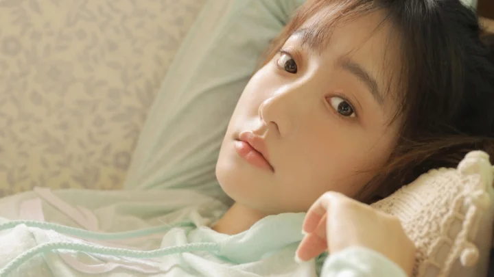 一名年轻女性侧卧在浅色 bedding 上，面部占据画面主要区域。