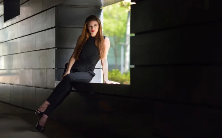 一名身穿黑色无袖服装的成年女性坐在现代建筑的开口处。