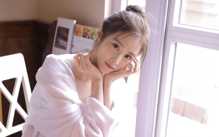 一位身穿白色上衣的女性靠在窗边，以手托脸看向镜头。