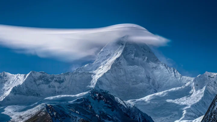 雪山峰顶被云层环绕，前景延伸着广阔的冰雪山地。