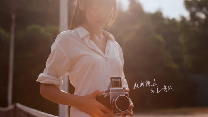一名穿白衬衫的成年女性在户外暖色阳光下手持复古相机。