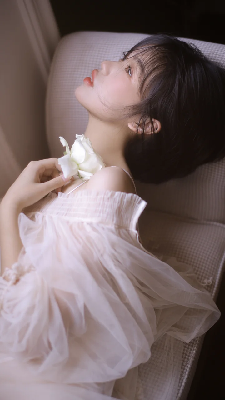 白いシアードレスを着た女性が椅子に横たわり、白い花を手にしています。