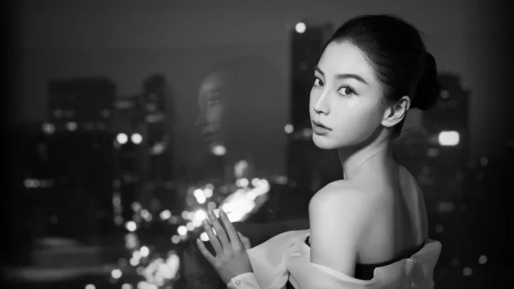 一位成年女性回望镜头，身后是黑白城市夜景与散景灯光。