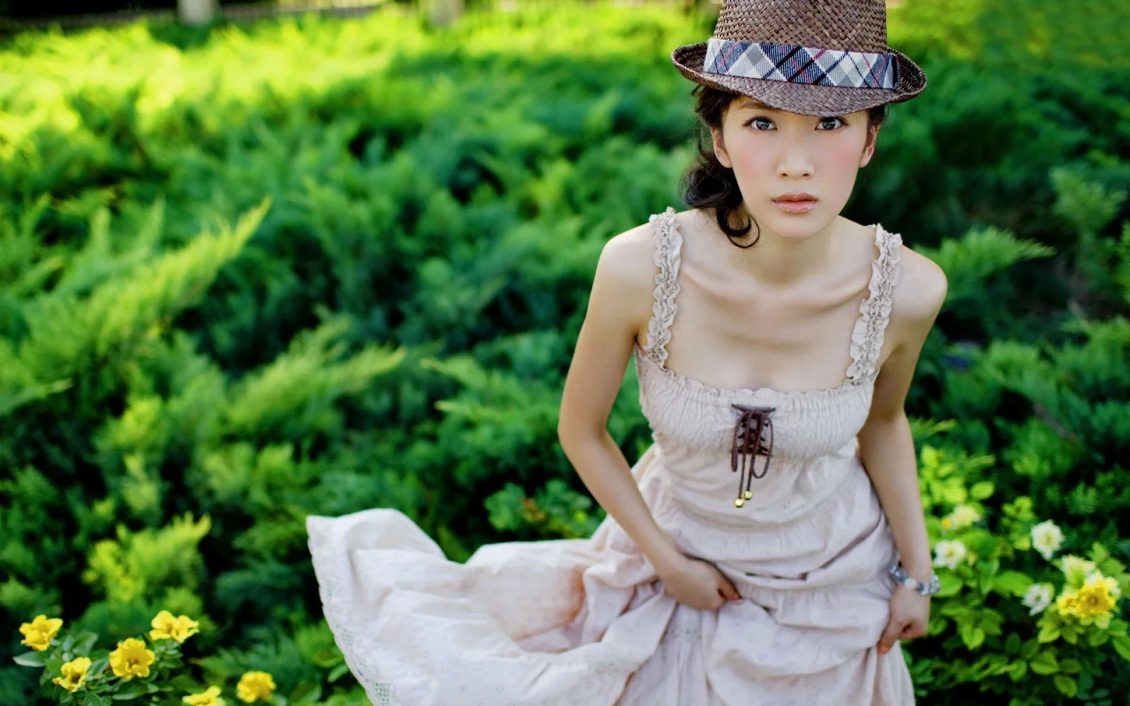 一名戴着帽子、穿着浅色连衣裙的女子坐在绿意盎然的花园中。