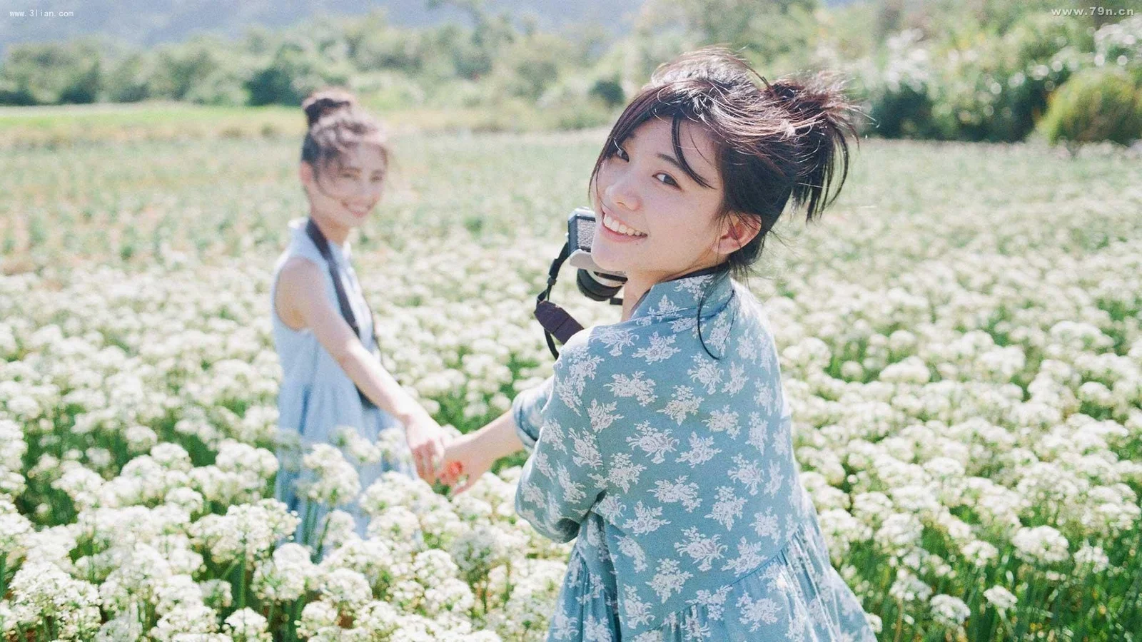 一名女子回头微笑，前方是盛开的白色花田，另一名女子站在她身后。