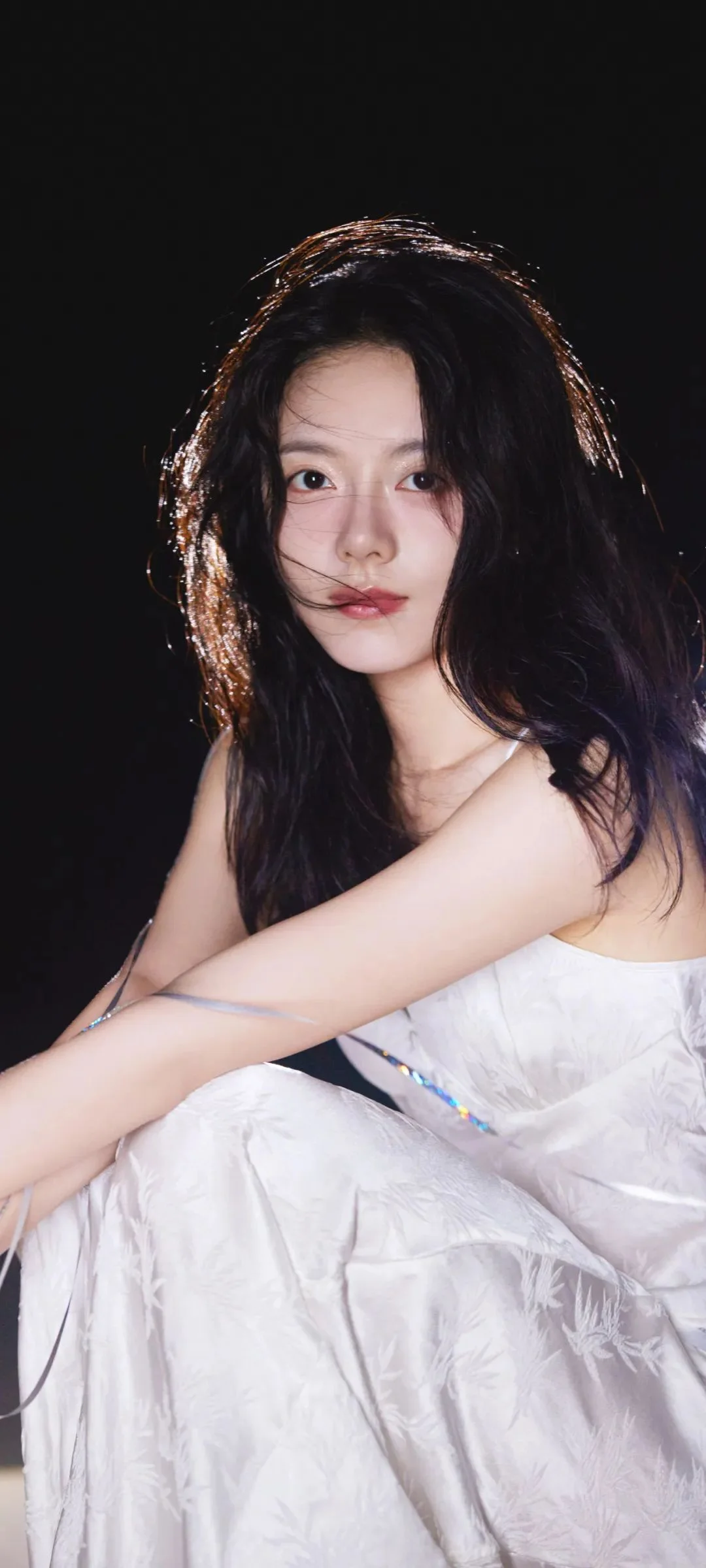 一名长发女性穿着白色礼服坐在黑色背景前。