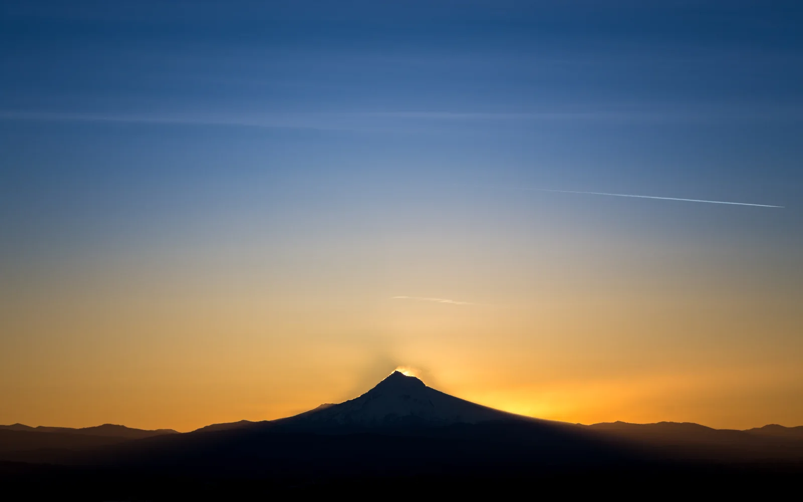 暮色天空下，一座山峰以深色剪影映衬着金橙色的夕阳余晖。