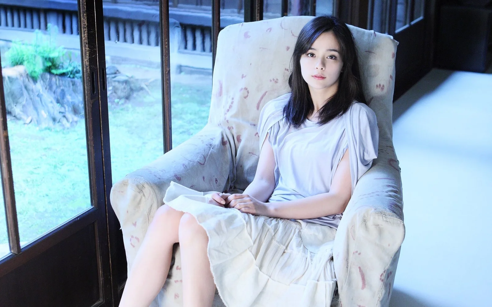 一名女性穿著淺色洋裝坐在窗邊的扶手椅上。