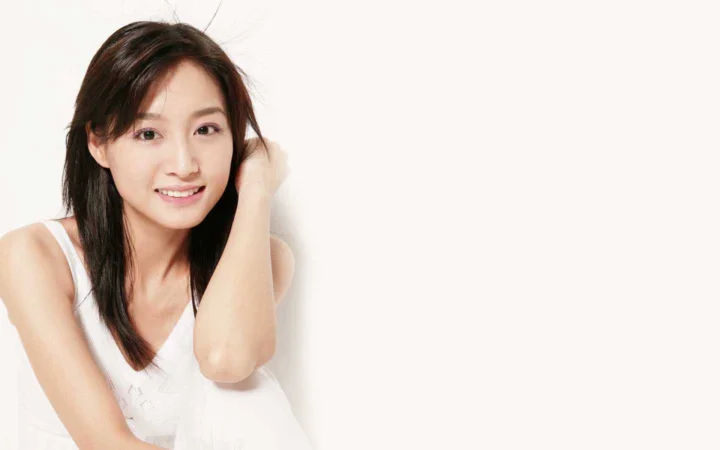 흰색 민소매 상의를 입은 성인 여성이 밝은 배경 앞에서 카메라를 향해 미소 짓고 있습니다.