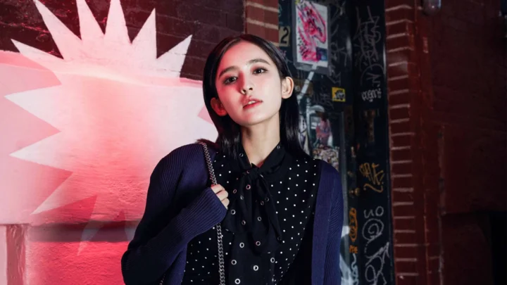 一名成年女性站在涂鸦墙前，红色灯光映照着街头背景。