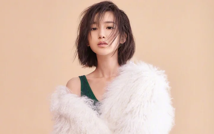 흰색 퍼 코트를 입은 성인 여성이 연한 갈색 배경 앞에서 인물 사진을 찍고 있다.