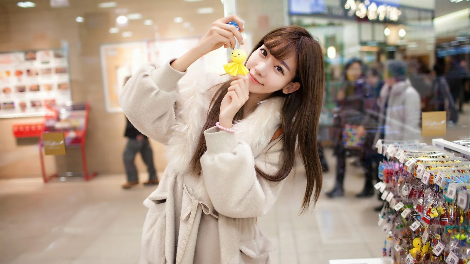 店内で女性が黄色い小さなおもちゃを手にしてカメラを見ている。