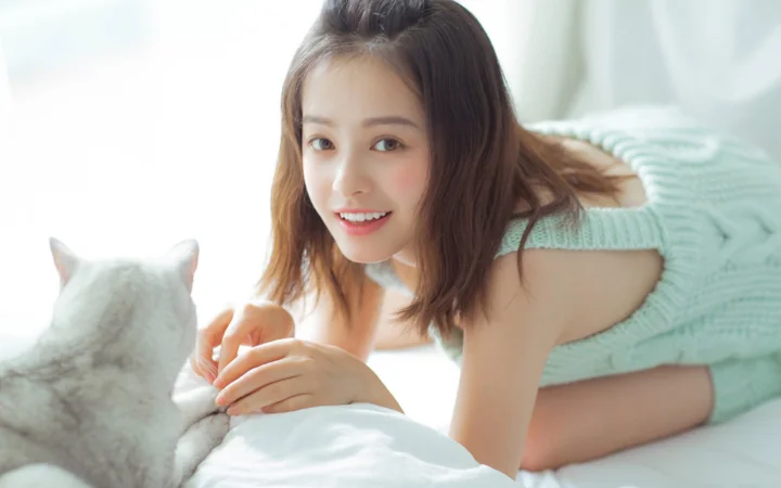 一名成年女性俯身在床上与一只猫互动。