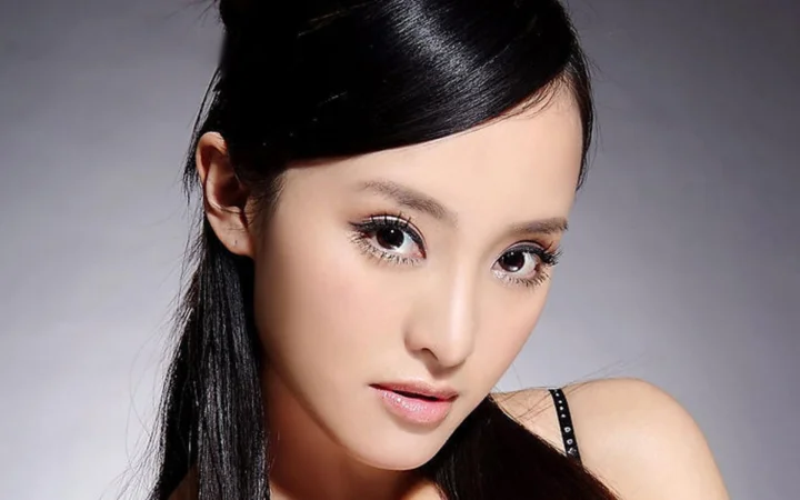 一位黑发女性在灰色背景前面向镜头展现精致妆容与面部特写。