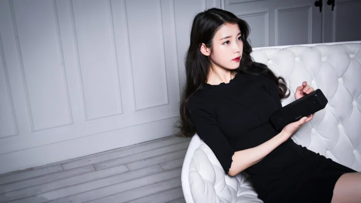 一名身穿黑色衣服的女性坐在白色沙发上，手持遥控器。