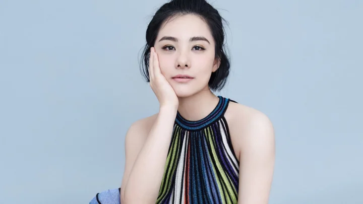 一名成年女性身穿条纹上衣，在蓝灰色背景前托腮注视镜头。