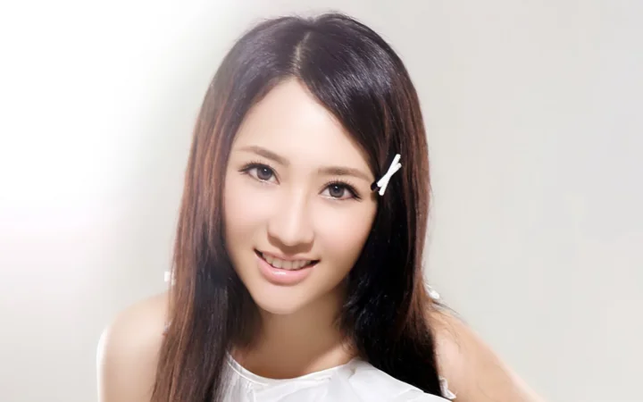 一位长发女性面带微笑，身穿白色上衣并佩戴发夹，正对镜头进行室内肖像拍摄。