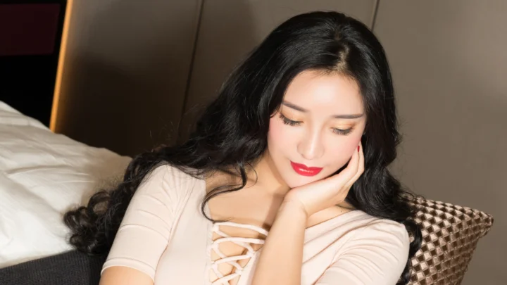 一名黑发女子倚靠在床上，用手托着脸颊。