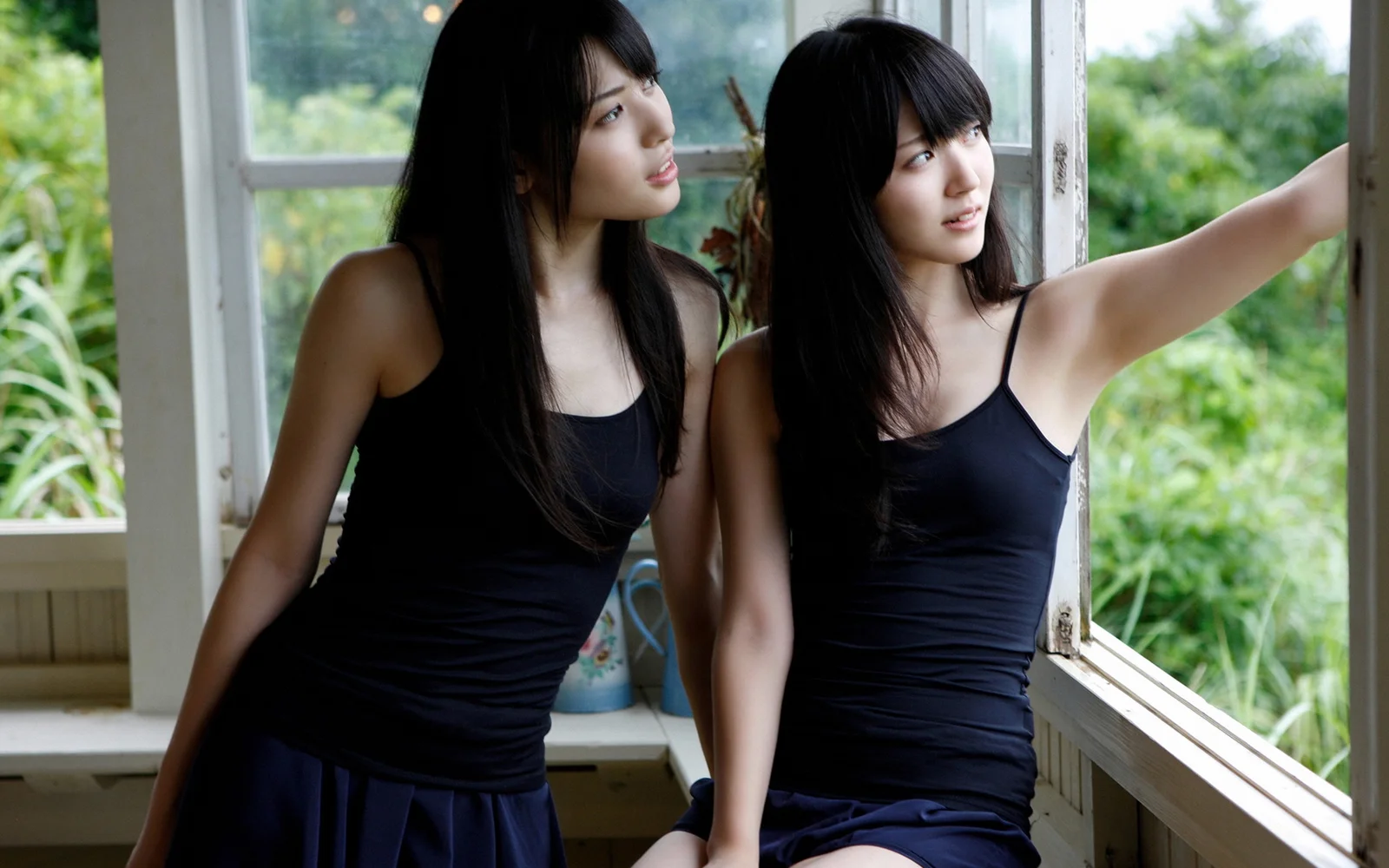 黒いノースリーブの服を着た二人の女性が室内の窓辺に立っています。