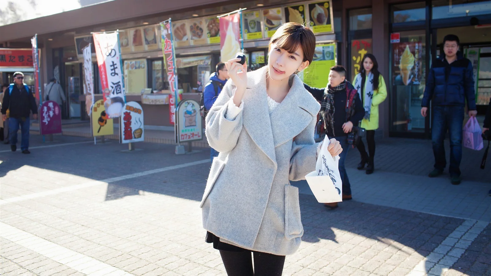 灰色のコートを着た女性が店先の通りに立っています。
