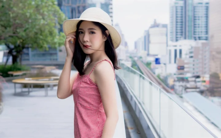 一名戴着宽檐帽的女子站在城市露台的玻璃栏杆旁。