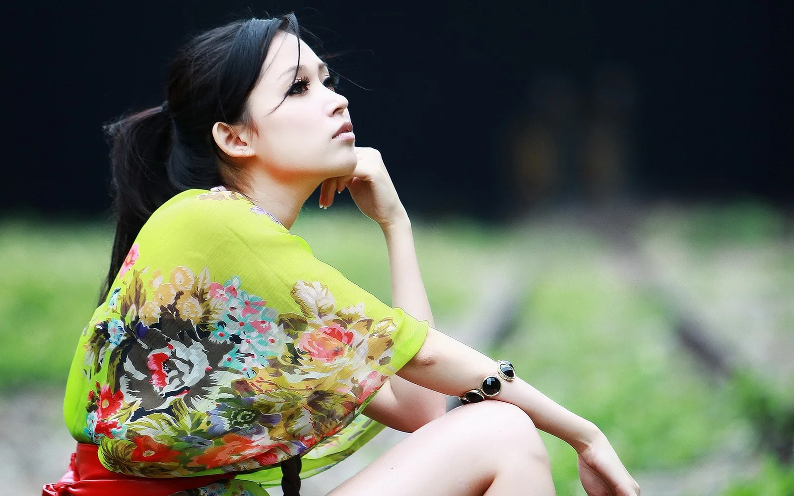 一名成年女性穿着花卉图案上衣坐在户外绿地前。