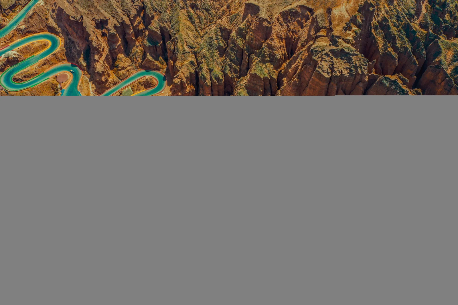 俯瞰视角展现了崎岖的峡谷山地和穿行其中的蜿蜒 turquoise 道路。