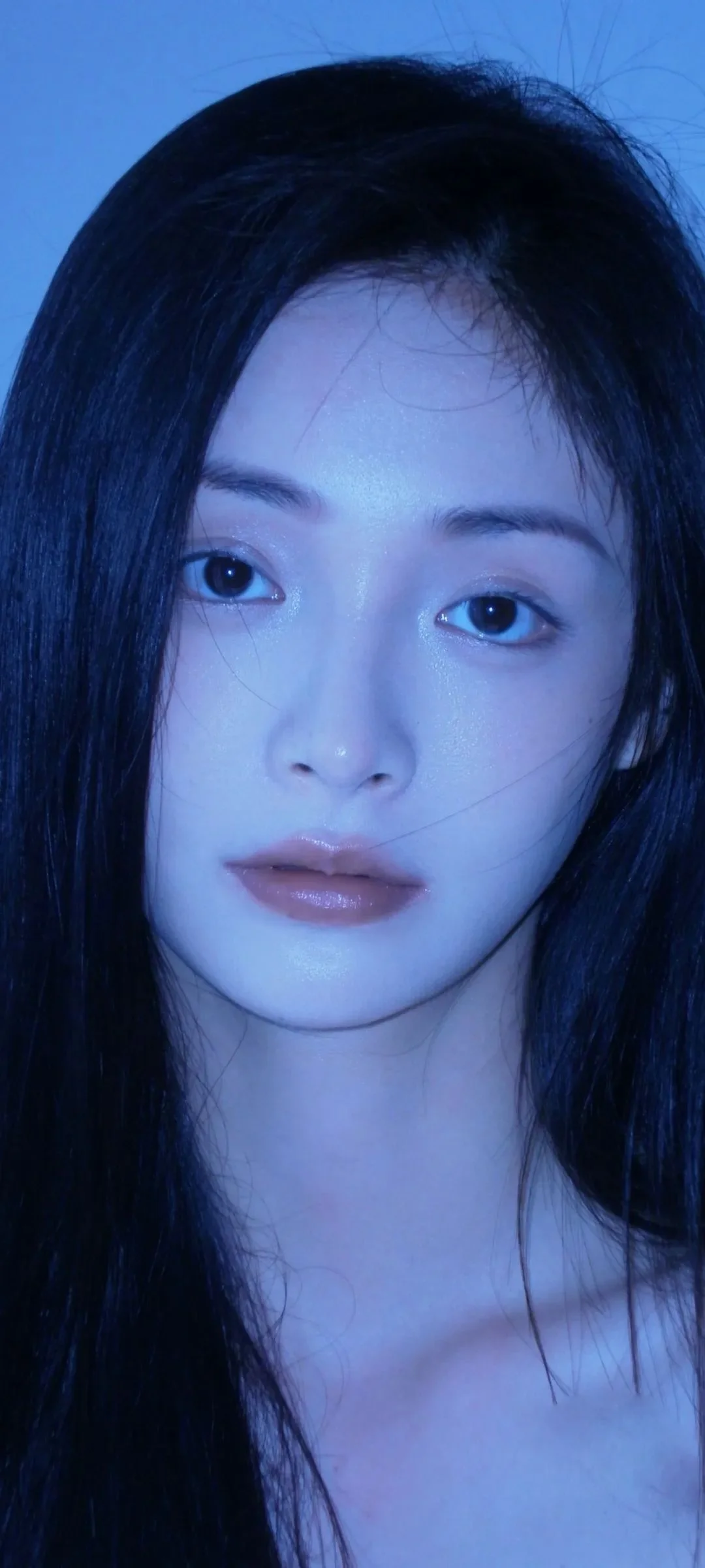 푸른 조명 아래 검은 머리 여성의 얼굴을 크게 담은 클로즈업입니다.