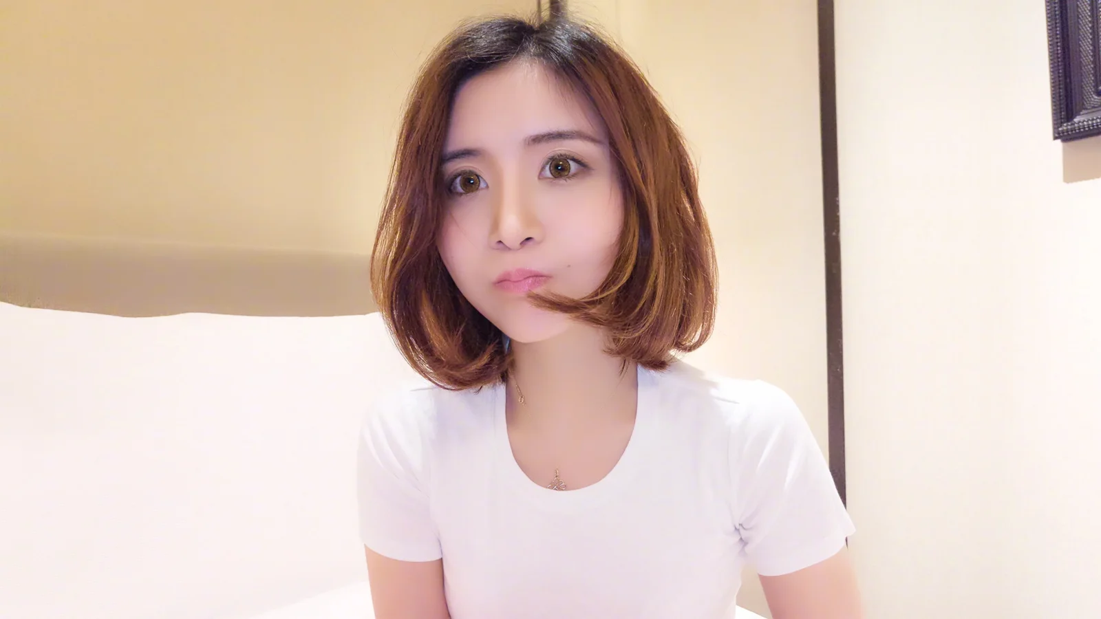 흰색 티셔츠를 입은 단발머리 여성이 실내 조명 아래에서 카메라를 바라보고 있습니다.