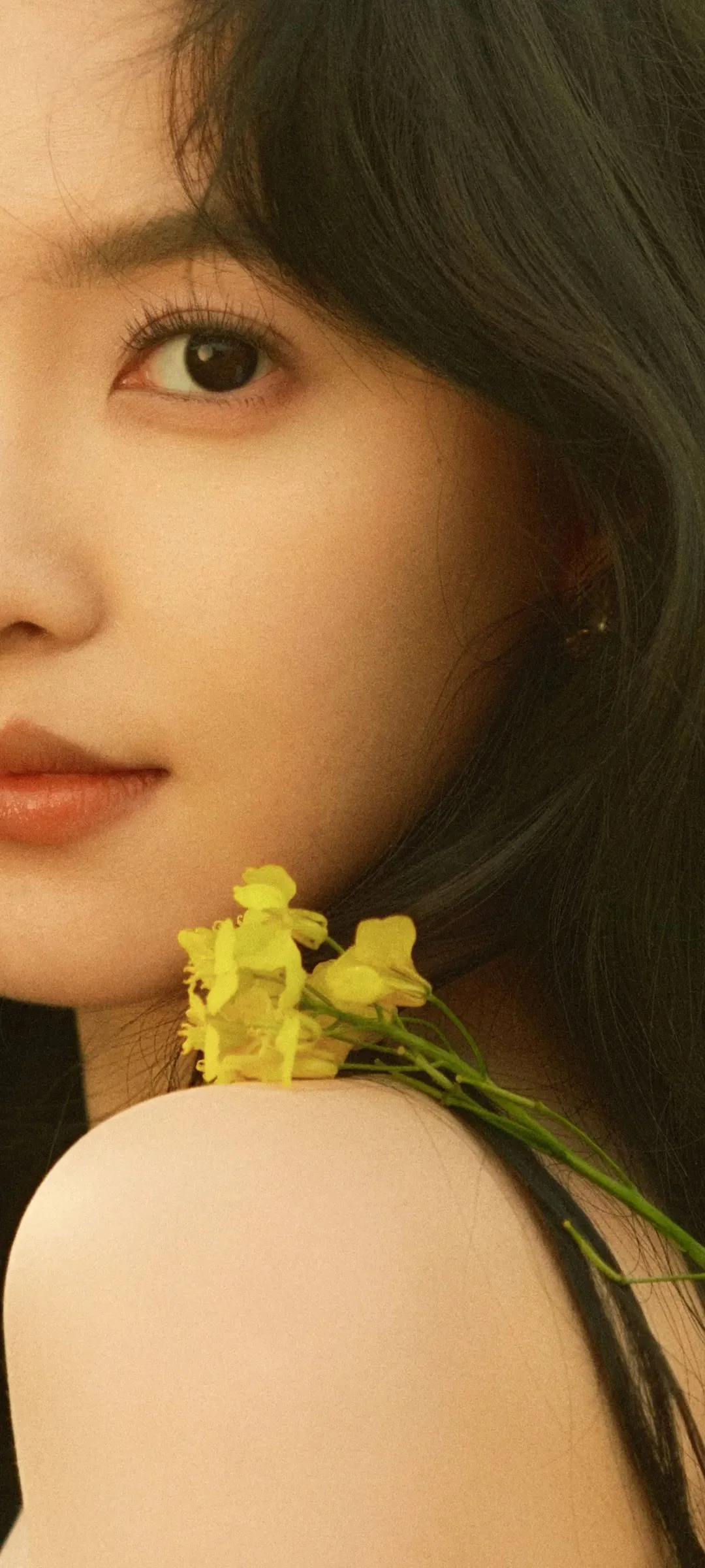 검은 머리 여성의 얼굴을 크게 담은 인물 사진으로 어깨 근처에 작은 노란 꽃다발이 보입니다.