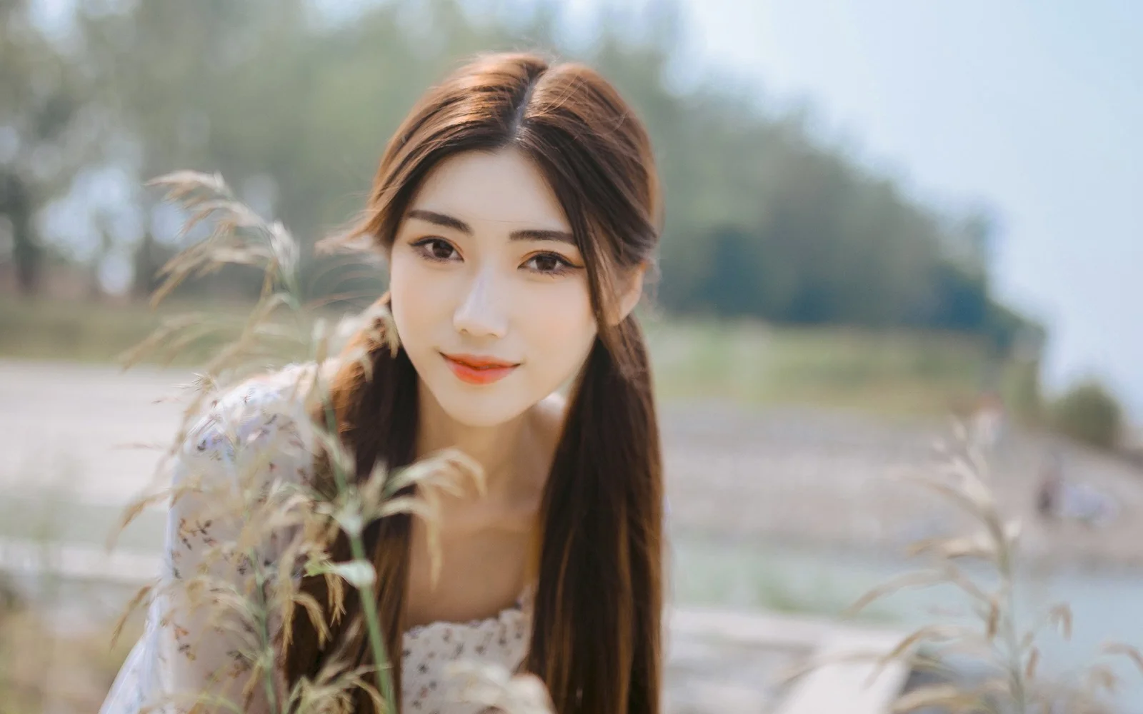 一名长发女性在户外植物前面向镜头微笑。