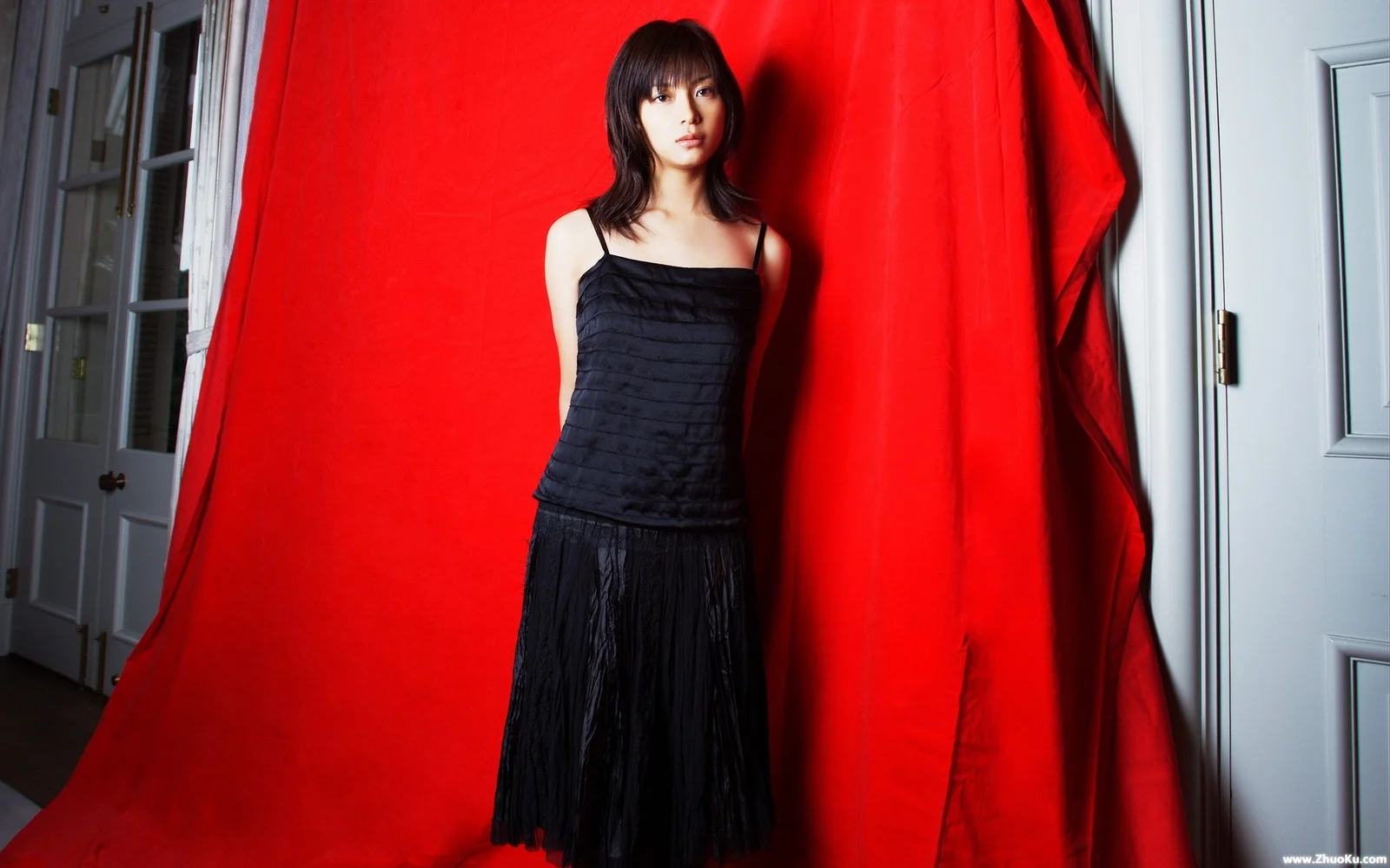 黒いドレスを着た女性が、室内の赤い背景の前に立っています。
