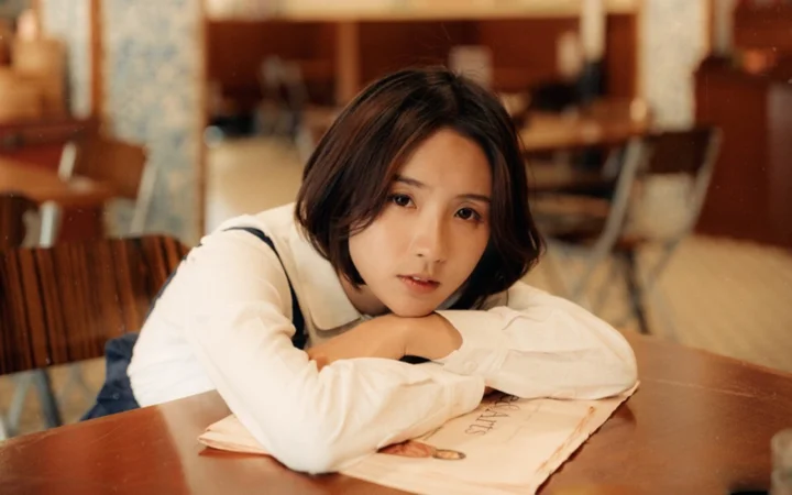 一名短发女子趴在咖啡馆的木桌上看向镜头。