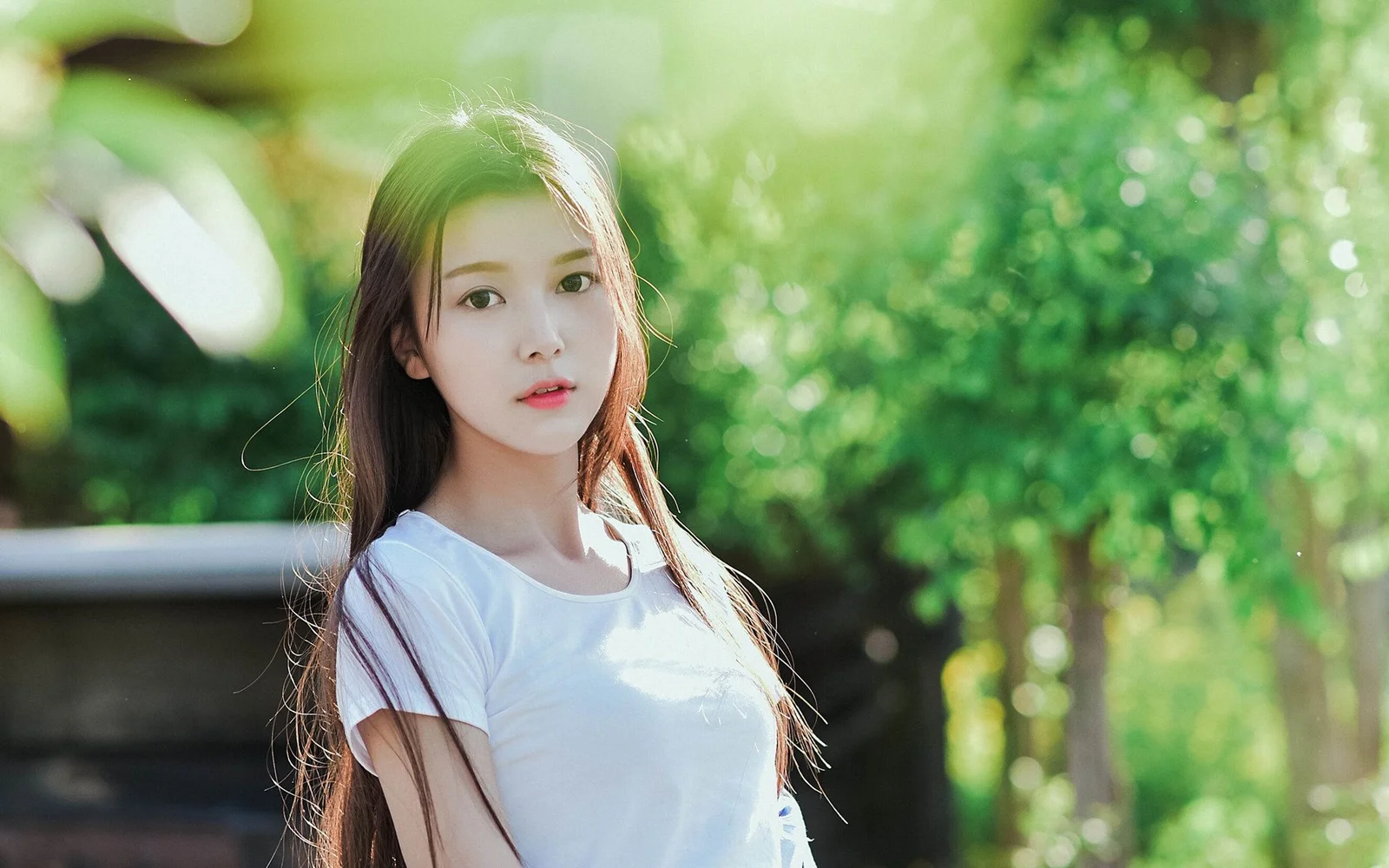 一位长发女性站在绿意盎然的户外阳光中。