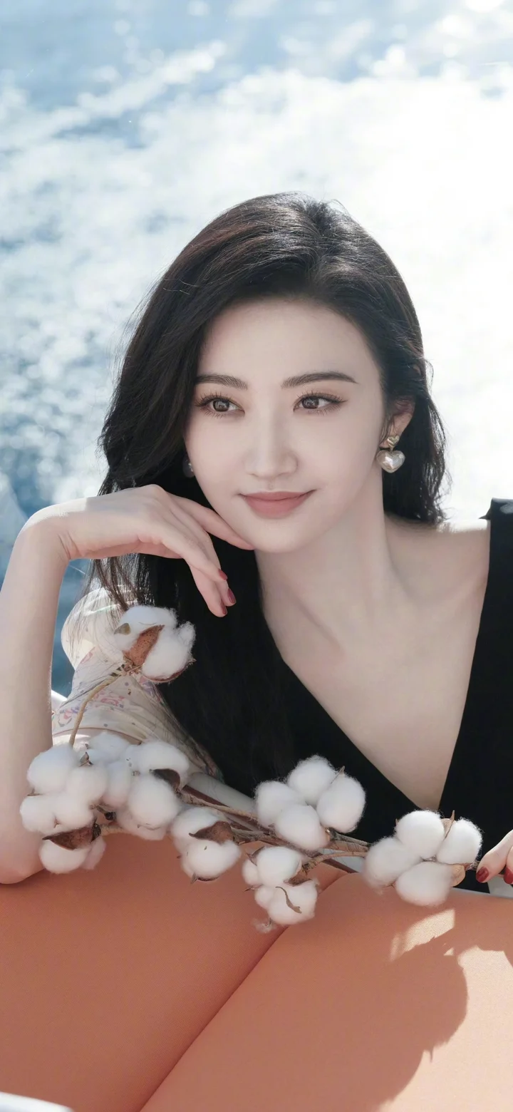 검은색 상의를 입은 여성이 목화 가지를 들고 밝은 야외 빛 속에서 카메라 가까이 미소 짓고 있다.