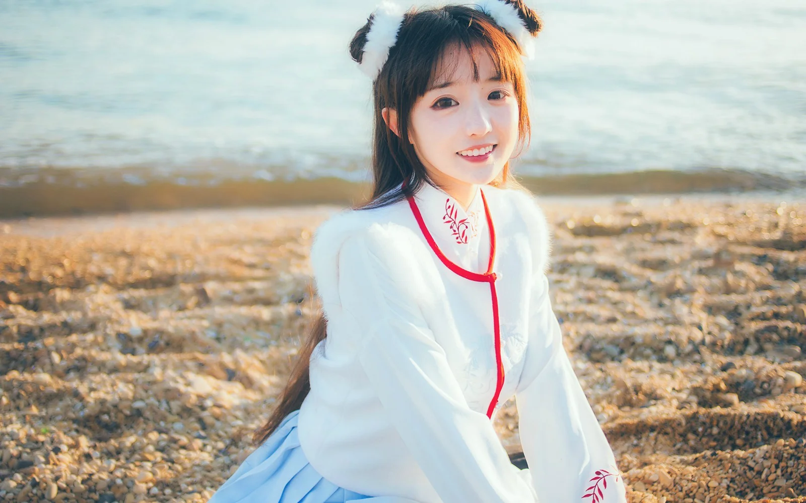 흰색 전통 의상을 입은 여성이 햇빛이 비치는 해변가에 앉아 있습니다.